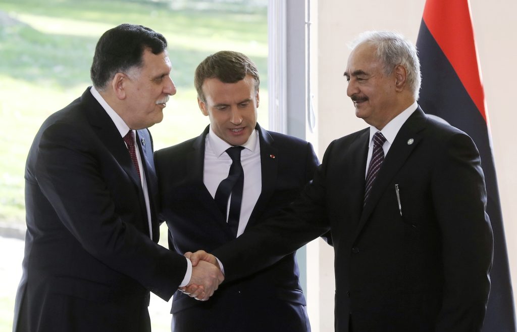 Emmanuel Macron (centro) osserva la stretta di mano fra  il premier libico Fayez al-Sarraj (sinistra) e il generale Khalifa Haftar (AFP)