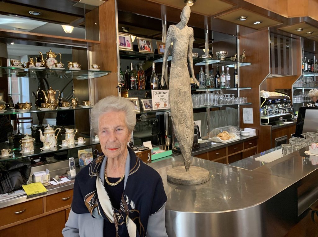 Livia Ravelli davanti al bancone del suo bar con una statua che la ritrae realizzata da Pedro Pedrazzini (M. Giacometti)