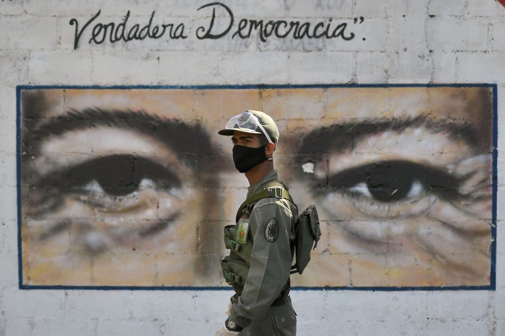 Un soldato sorveglia un seggio elettorale con gli occhi del defunto presidente Chavez dipinti sul muro alle sue spalle. La scritta «Vera democrazia» sembra una beffa. (Keystone)