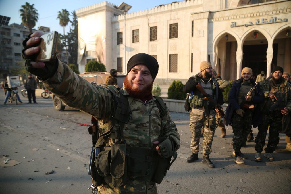 Combattenti guidati dal gruppo militante islamista Hayat Tahrir al-Sham davanti a un ufficio del Governo siriano nella città di Hama (Keystone)